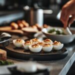 A warm, inviting modern kitchen scene featuring a variety of beautifully styled deviled egg dishes arranged on a countertop, surrounded by fresh ingredients like herbs and spices. The image includes cooking tools such as utensils, mixing bowls, and a cutting board, with soft, natural lighting creating a cozy atmosphere that reflects a passion for cooking. The background showcases a hint of kitchen decor, adding a homely yet professional touch without focusing on a single dish.